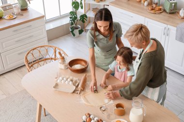 Annesi ve büyükannesiyle mutfakta kurabiye yapan küçük bir kız.