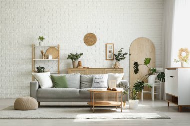 Gri kanepe, ahşap masa ve bitkilerle aydınlık oturma odasının içinde.