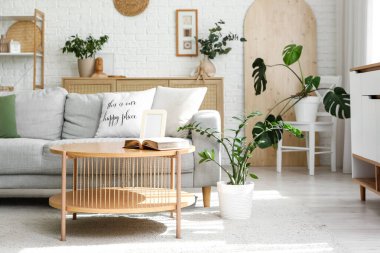 Gri kanepe, ahşap masa ve bitkilerle aydınlık oturma odasının içinde.