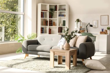 Gri kanepesi, masaları ve kitaplığı olan aydınlık oturma odasının içinde.