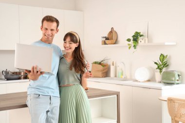 Genç çift mutfakta dizüstü bilgisayar kullanıyor.