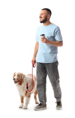 Kahve fincanı olan genç bir adam ve beyaz arka planda yürüyen bir Avustralya çoban köpeği.