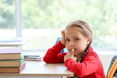 Sınıfta masa başında tırnak yiyen küçük bir kız.