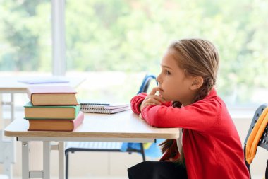 Sınıfta masa başında tırnak yiyen küçük bir kız.