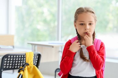 Sınıfta tırnaklarını yiyen küçük bir kız öğrenci.