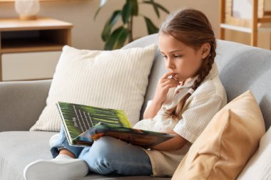 Evde kanepede kitap okuyan küçük bir kız.