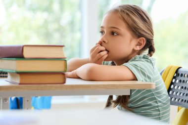 Sınıfta masa başında tırnak yiyen küçük bir kız.