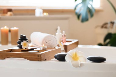 Mumlu havlular, spa taşları ve beyaz Plumeria çiçekleri kuafördeki küvette duruyor.