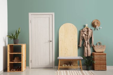 Raflar, ahşap tezgah, ev bitkileri, bankta ayakkabılar ve mavi duvarda asılı sonbahar ceketi olan modern koridorun içi.