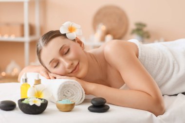 Beyaz tesisat çiçekleri, spa taşları, deniz tuzu ve kozmetik yağı salonda kanepede uzanan güzel, genç ve mutlu bir kadın.
