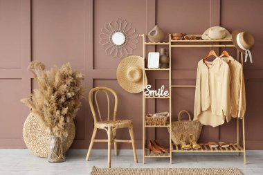 Modern koridorun içinde elbise askısı, ayakkabı standı, kuru çiçekler, kahverengi duvarın yanındaki raflarda sandalye ve ev dekorasyonu.