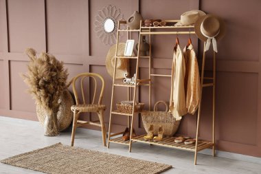 Modern koridorun içinde elbise askısı, ayakkabı standı, kuru çiçekler, kahverengi duvarın yanındaki raflarda sandalye ve ev dekorasyonu.