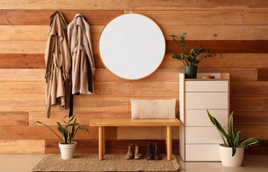 İçinde raf ünitesi, ayna, bank, ev bitkileri, ayakkabılar ve kahverengi ahşap duvarda asılı ceketler olan modern koridorun içi.