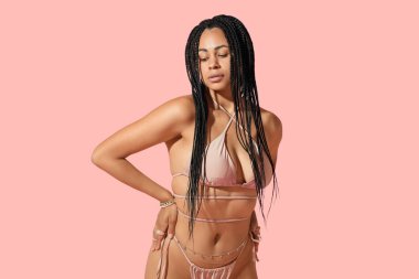 Pembe arka planda aksesuarları olan bikinili güzel Afro-Amerikalı bir kadın.