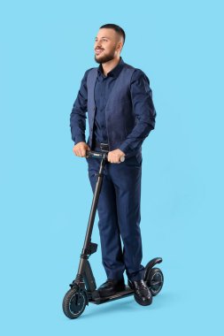Mavi arka planda elektrikli scooter kullanan takım elbiseli genç adam.