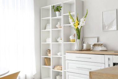 Mutfak tezgahında gladiolus çiçekli vazo ve çaydanlık.