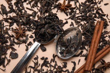 Kuru siyah çay yaprakları ve bej arka planda tarçın ile infüzör kaşık