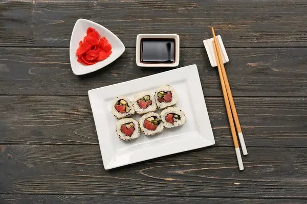 Soya soslu lezzetli suşi ruloları, yemek çubukları ve ahşap arka planda marine edilmiş zencefil.
