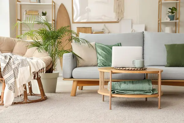 Aydınlık oturma odasının içinde gri kanepe ve sehpanın üzerinde modern dizüstü bilgisayar.