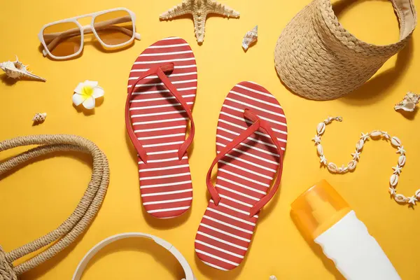 Şık plaj ayakkabılarıyla kompozisyon, bir şişe güneş kremi ve sarı arka planda aksesuarlar, yakın plan.