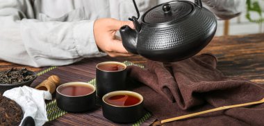 Ahşap masada demlikten puer çay dolduran kadın, yakın plan.