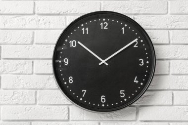 Beyaz tuğlalı duvarda siyah şık bir saat.