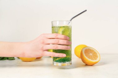 Beyaz arka planda bir bardak limonata, limon ve saman olan bir kadın eli.