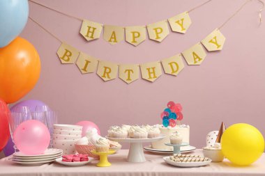Farklı şekerlemeler ve pembe duvarlı bir doğum günü partisi için dekorasyon masası.