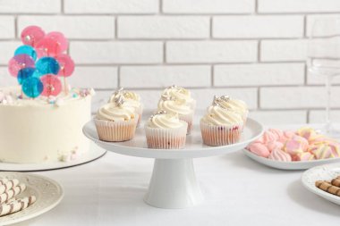 Beyaz keklerle tatlı standı ve doğum günü partisi için diğer tatlılar beyaz tuğla duvara karşı masada.