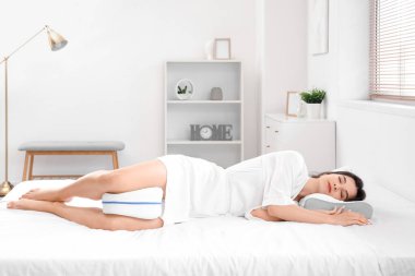 Yumuşak ortopedik yastıklı pijamalı genç bir kadın. Evdeki rahat yatakta bacakları için.