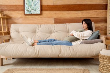 Oturma odasındaki rahat koltukta yastıklı genç kadın dinleniyor.