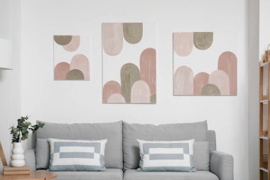 Oturma odasının içinde rahat bir kanepe, çiçek ve beyaz duvarda resimler var.