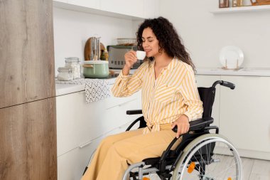 Tekerlekli sandalyedeki genç Afro-Amerikalı kadın evinde bir fincan kahveyle
