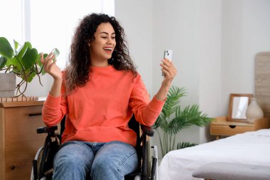 Evinde cep telefonu olan tekerlekli sandalyedeki genç Afro-Amerikalı kadın.