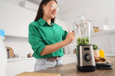 Genç Asyalı kadın mutfakta blendere süt döküyor.