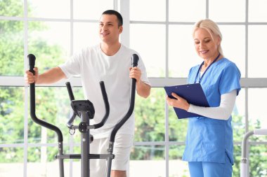 Rehabilitasyon merkezinde genç bir adamla egzersiz yapan kadın fizyoterapist.