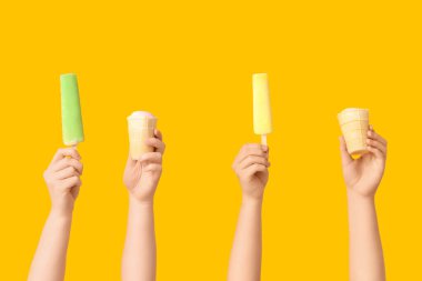 Sarı arka planda farklı tatlı dondurmalı kadın elleri.