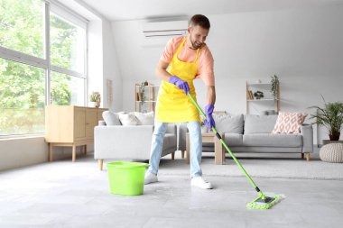 Erkek hademe, ışık odasında paspasla yerleri temizliyor.