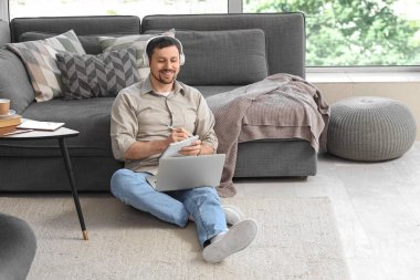 Dizüstü bilgisayarı ve not defteri olan genç erkek öğretmen evde online ders veriyor.