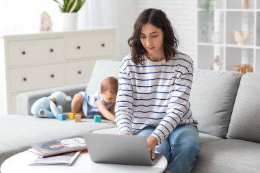 Evde doğum izninde dizüstü bilgisayarla çalışan tatlı bebek ve genç anne.