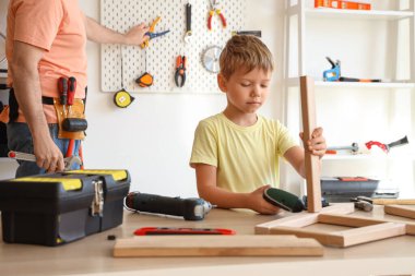 Babası ve küçük oğlu farklı enstrümanlarla evde mobilya monte ediyorlar.