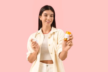 Pembe arka planda farklı B vitamini hapları olan genç bir kadın.