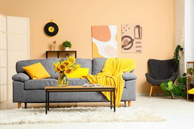 Oturma odasının iç tarafında ayçiçekleri olan rahat bir kanepe ve kahve masası.