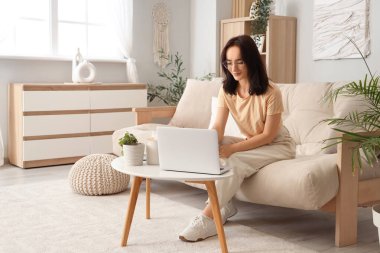 Evdeki masada dizüstü bilgisayar kullanan genç bir kadın.