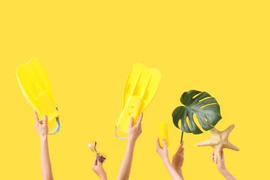 Palet, güneş gözlüğü, güneş kremi, sarı arka planda canavar yaprağı ve deniz yıldızı olan kadın eller. Seyahat kavramı