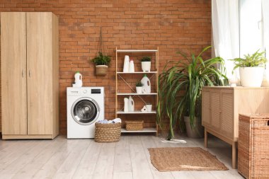 Çamaşır makinesi, sepeti ve raf ünitesi olan çamaşır odasının içi.