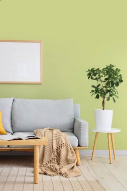 Yeşil duvarın yanındaki yastıklı, çiçekli ve kahve masalı şık gri kanepe.