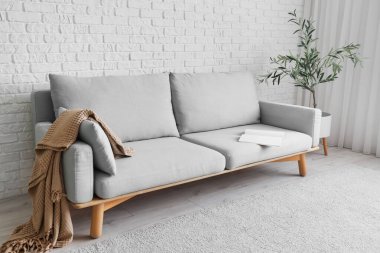 Beyaz tuğla duvarın yanında çiçekli şık gri kanepe.