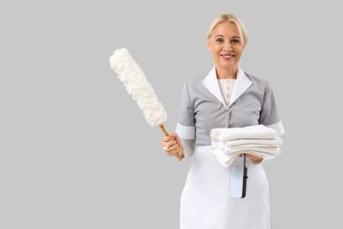 Gri arka planda pp-toz bezi ve temiz havlu yığınıyla orta yaşlı oda hizmetçisi.