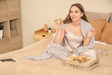 Evde pijamalı, pizza yiyen genç ve güzel bir kadın.